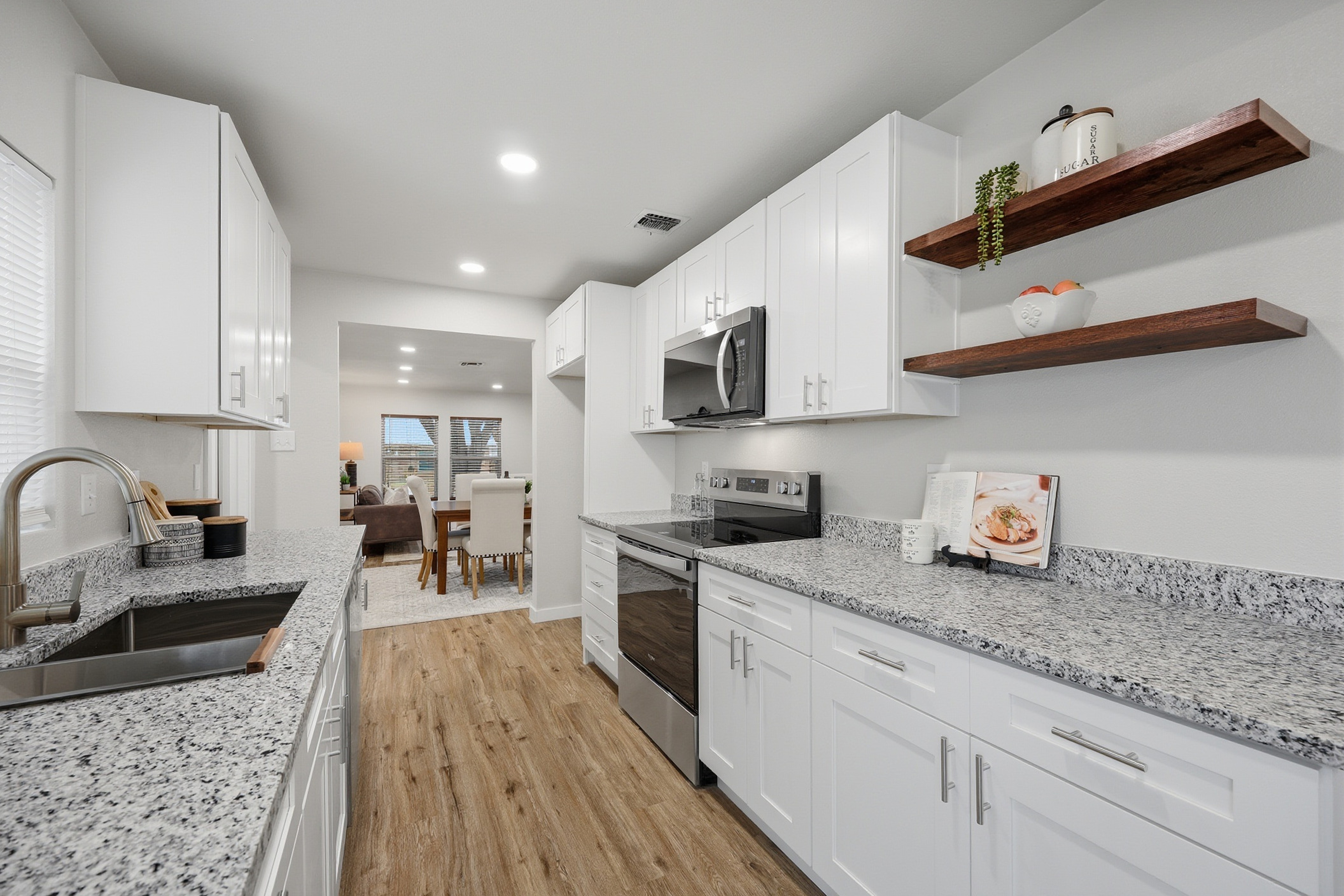 Renovated kitchen with white shaker cabinets, granite countertops, and floating wood shelves